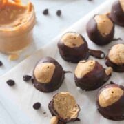 High protein peanut butter chocolate buckeyes on top of a parchment paper, with peanut butter on the side.