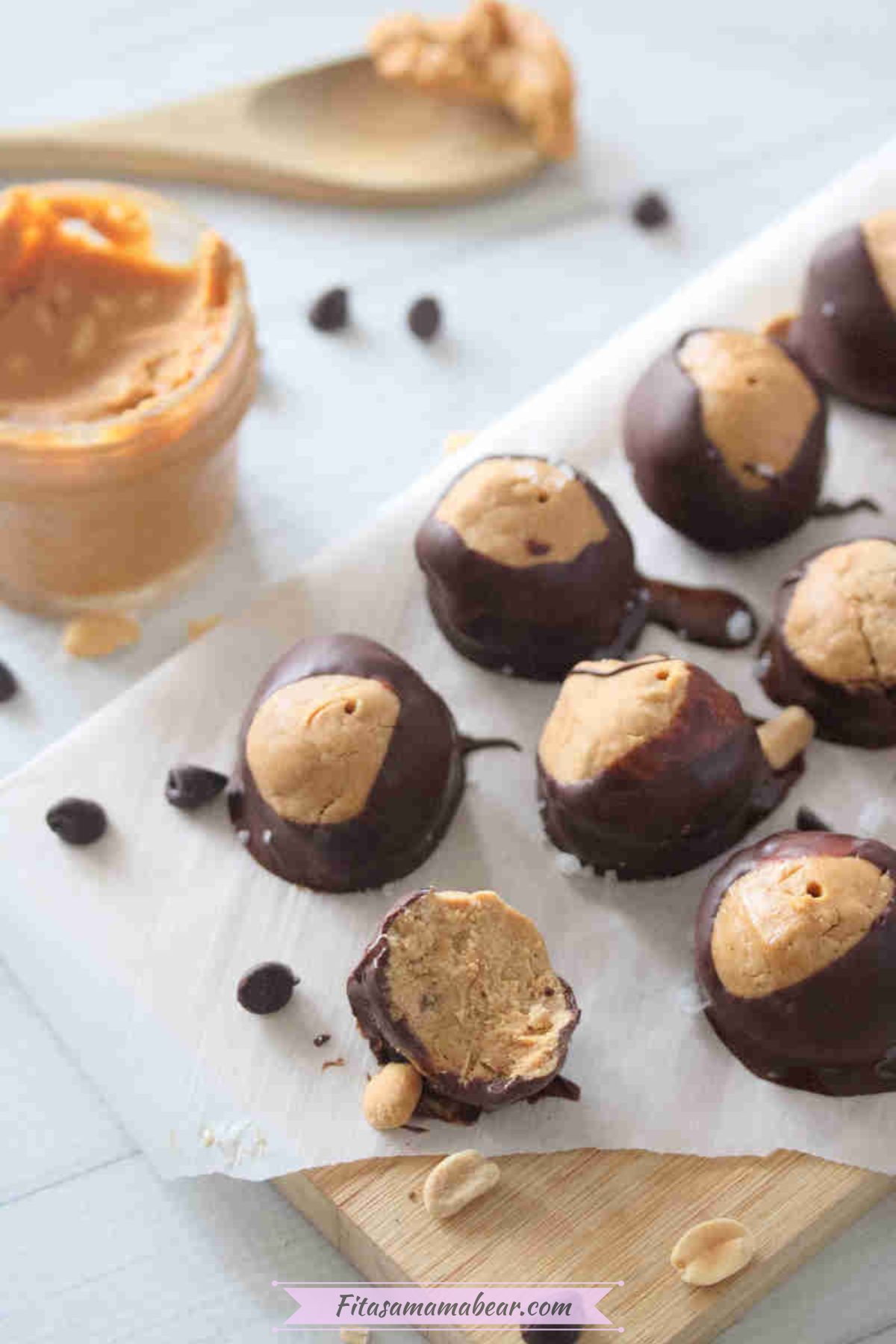High protein peanut butter chocolate buckeyes on top of a parchment paper, with peanut butter on the side.