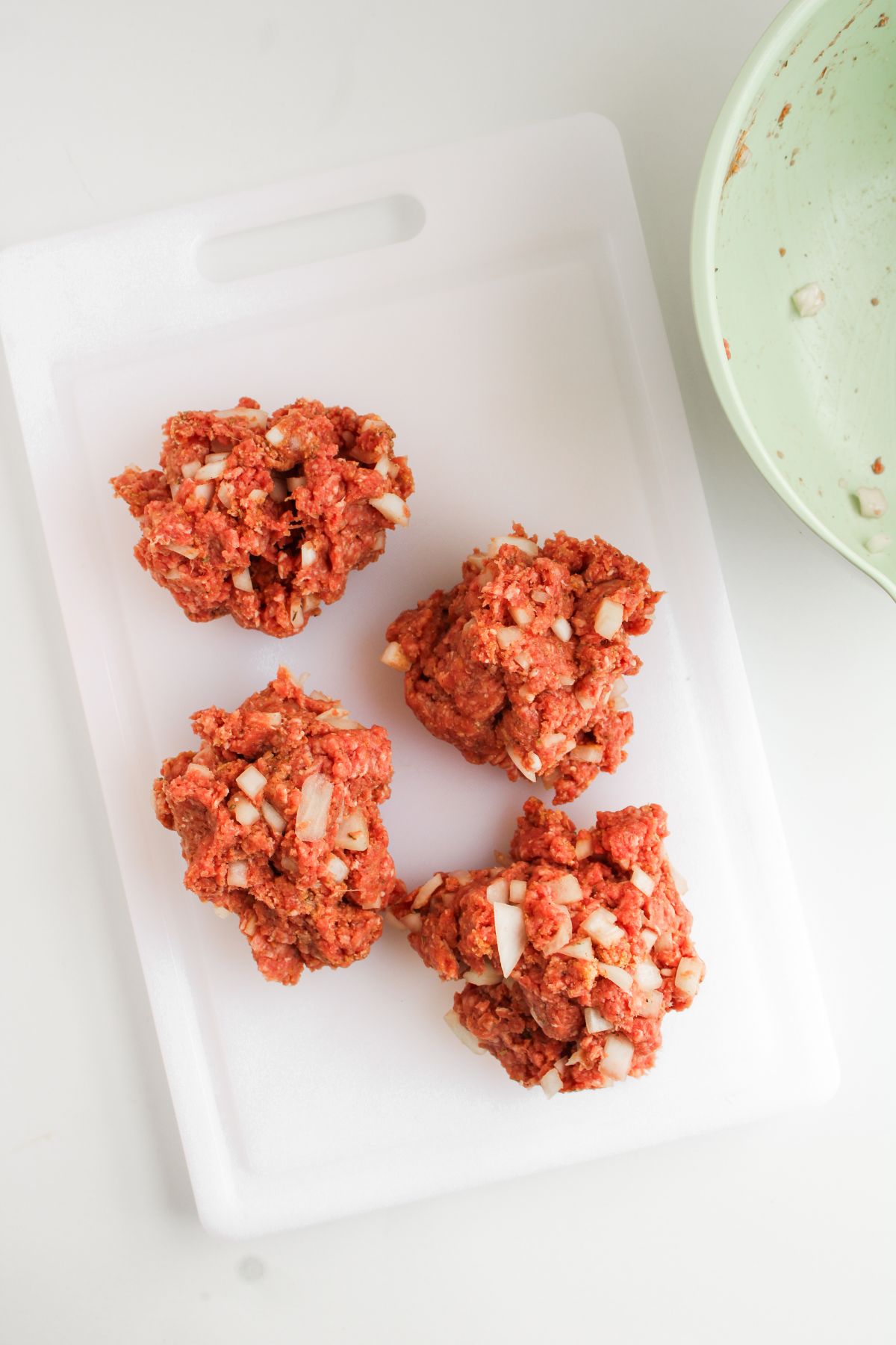 Ground beef formed into mini meat loaves on top of a plastic chopping board.