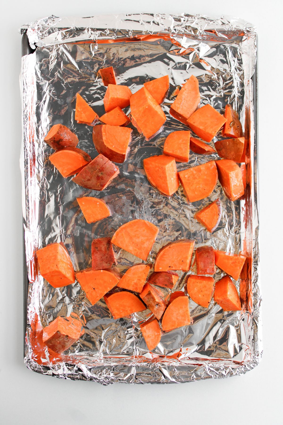 Sliced sweet potatoes in a sheet pan with foil.