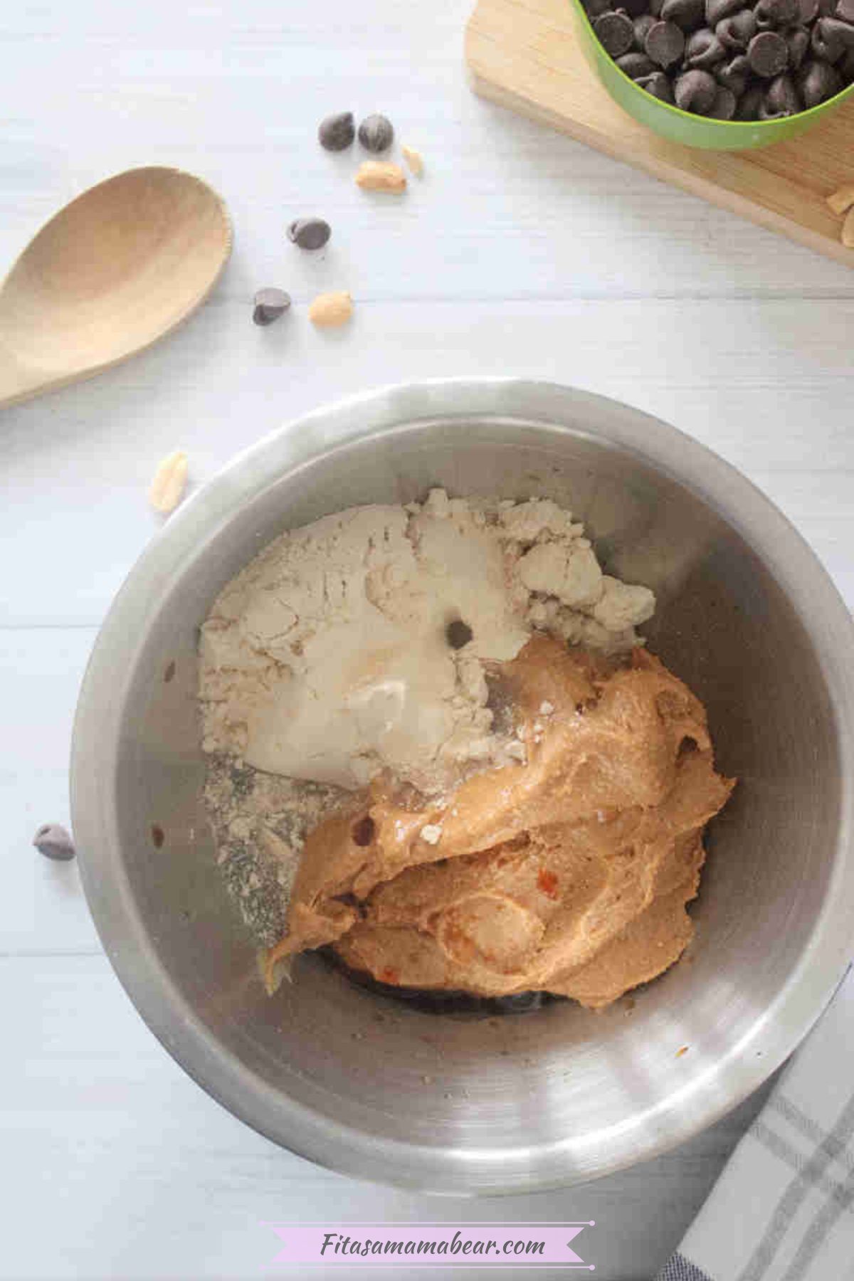 Peanut butter, protein powdr, vanilla extract, and maple syrup mixed in a stainless steel bowl.