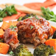 Baked meat loaf with barbecue glaze and roasted broccoli and sweet potatoes on a plate.