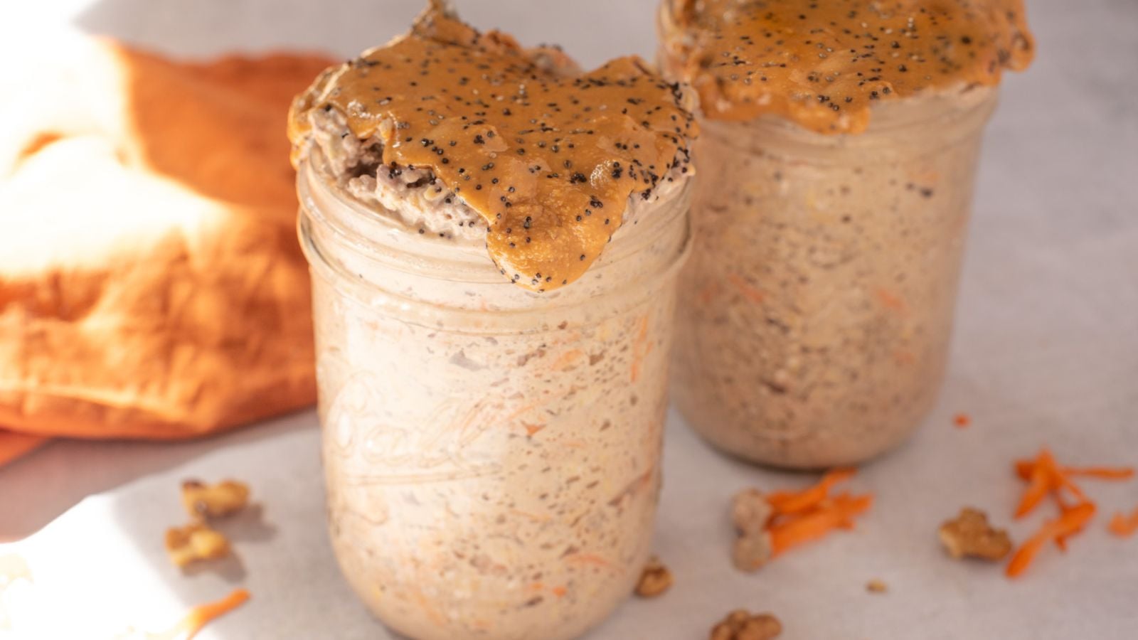 Two mason jars with carrot cake overnight oats topped with nut butter and chia seeds.