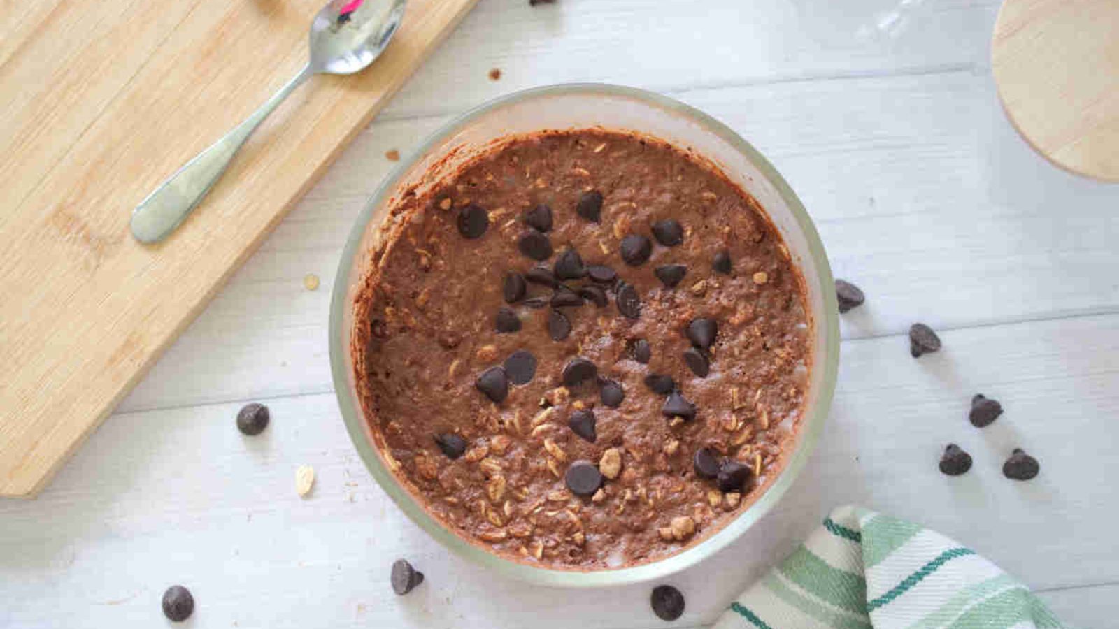 Large bowl with chocolate protein overnight oats topped with chocolate chips and a cutting board and chocolate chips around it.