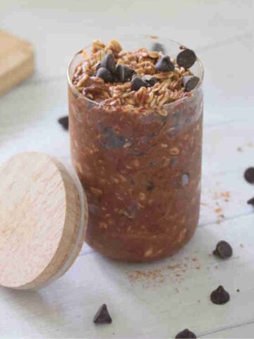 Small jar with chocolate protein overnight oats topped with chocolate chips and a lid beside it.