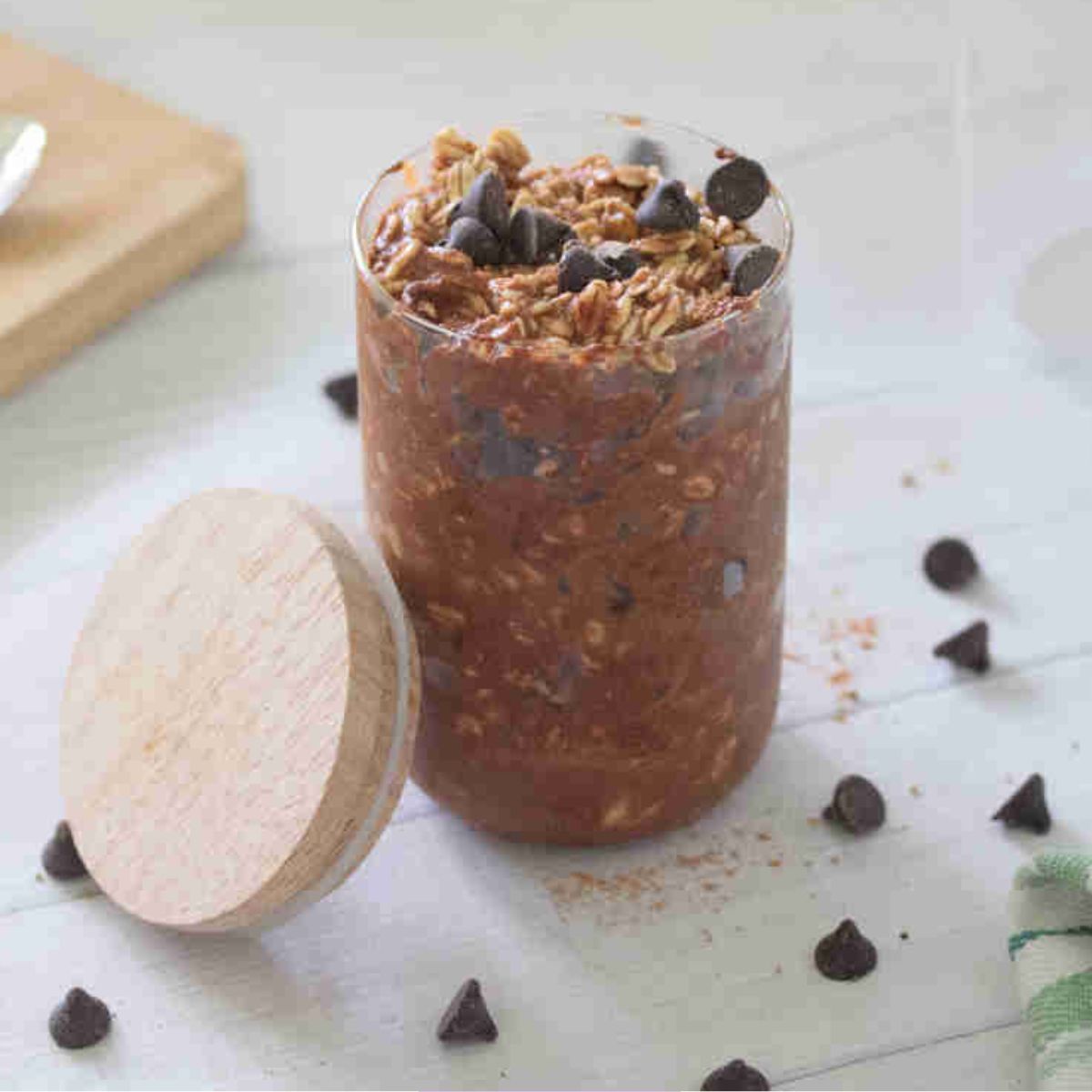 Small jar with chocolate protein overnight oats topped with chocolate chips and a lid beside it.