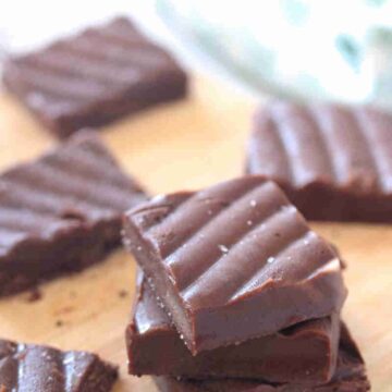 Squares of coffee fudge stacked and on on a cutting board.