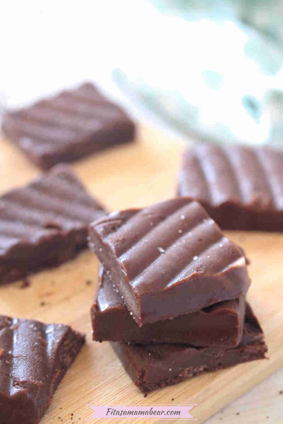 Squares of coffee fudge stacked and on on a cutting board.