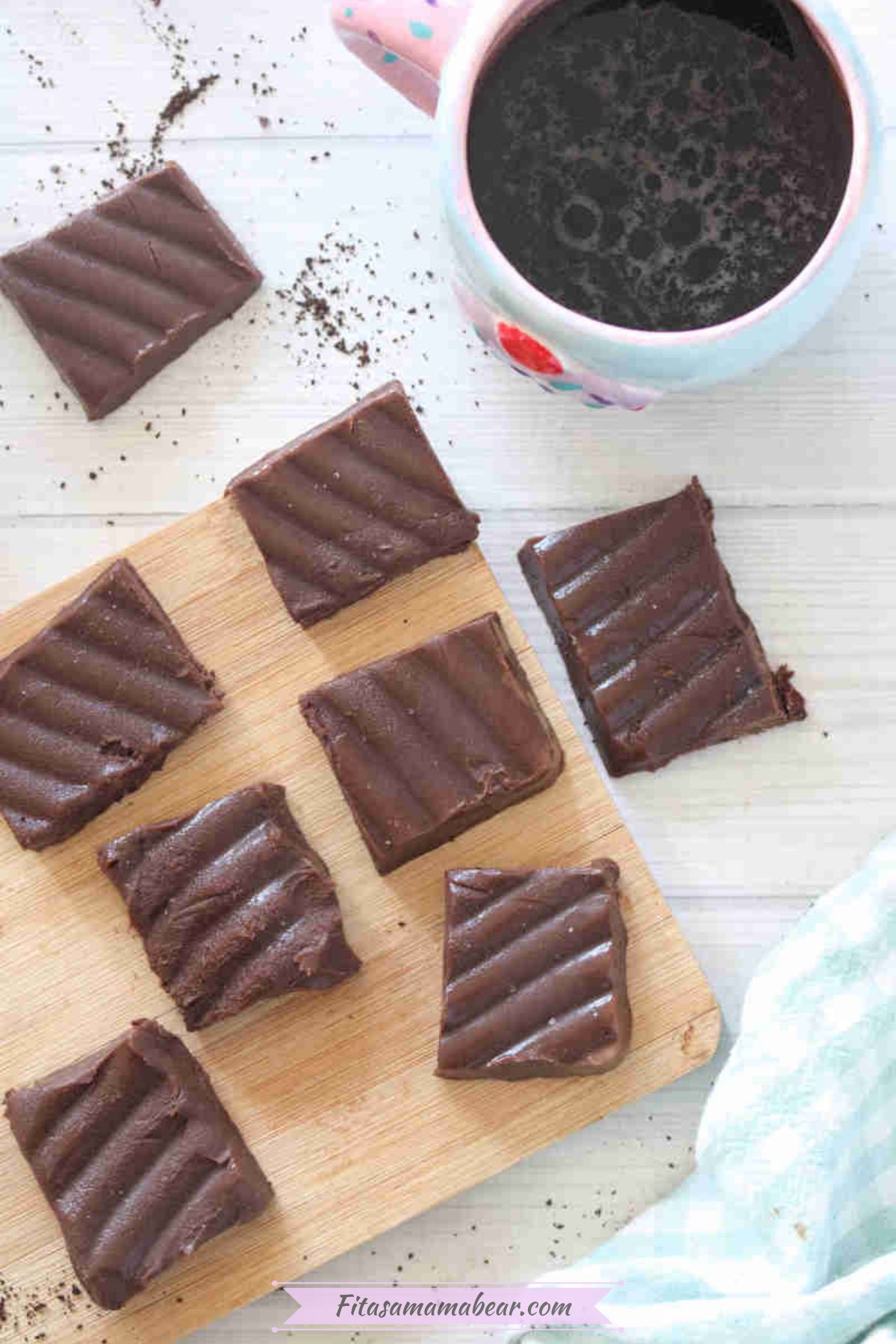 Squares of coffee fudge on a cutting board with a cup of coffee beside it.