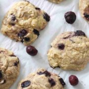 Cherry muffin tops on a piece of parchment paper with frozen cherries around them.