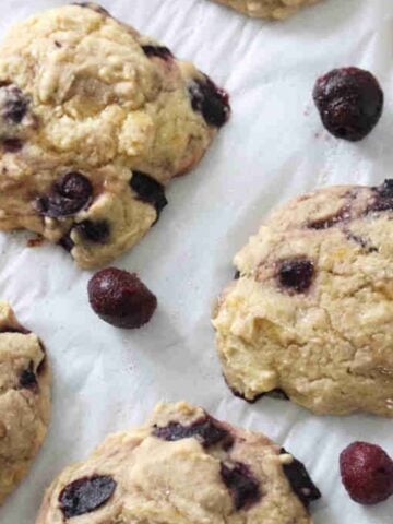 Cherry muffin tops on a piece of parchment paper with frozen cherries around them.