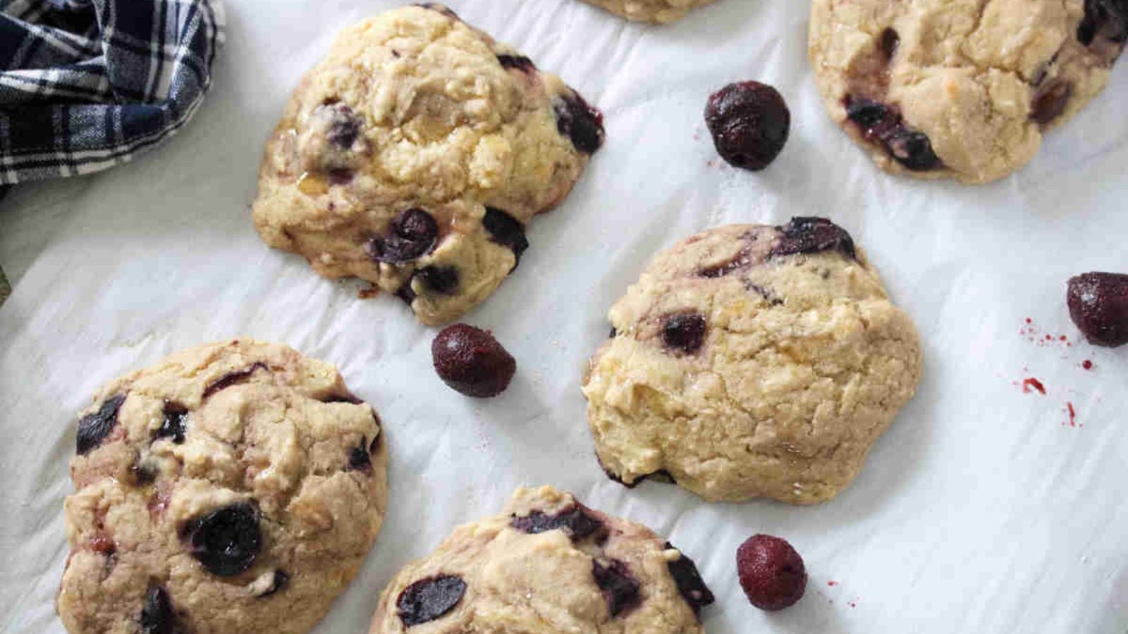 Cherry muffin tops on a piece of parchment paper with frozen cherries around them.