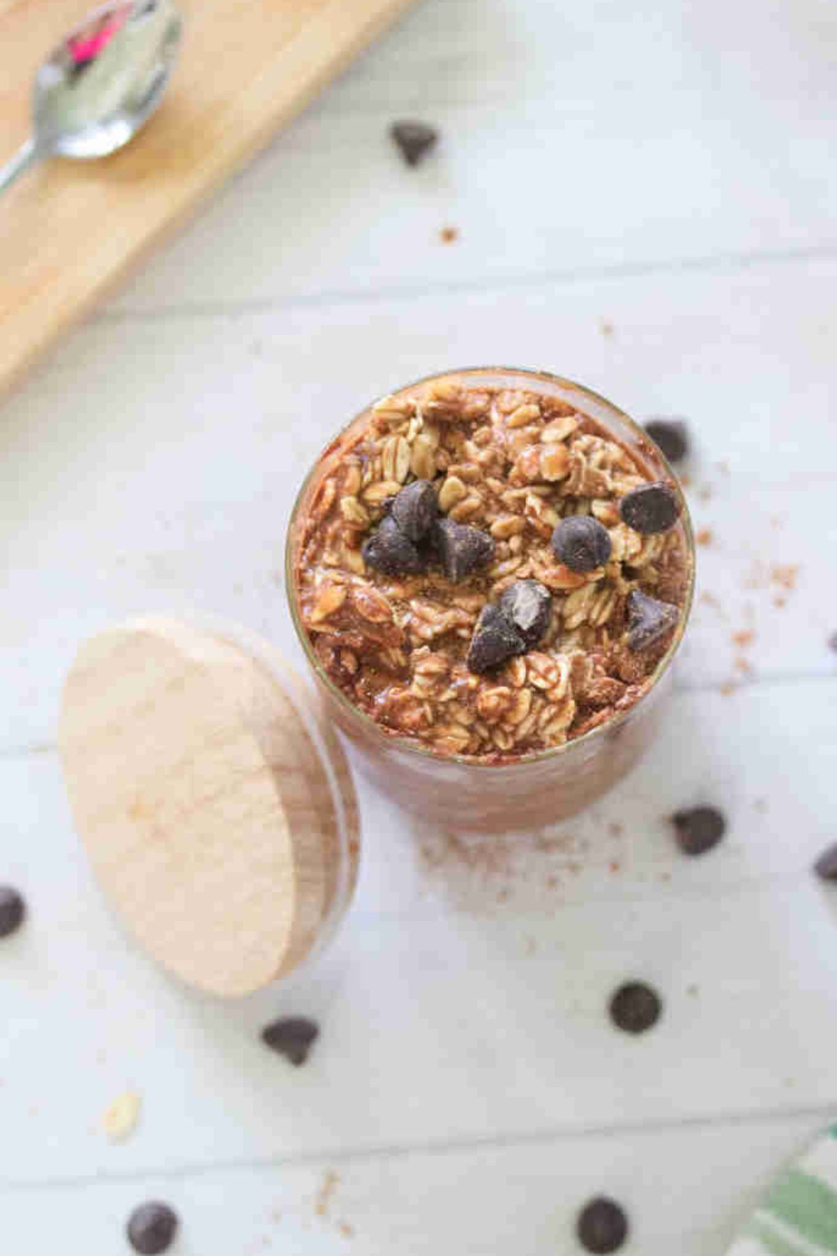 Small jar with chocolate protein overnight oats topped with chocolate chips and a lid beside it and chocolate chips around it.