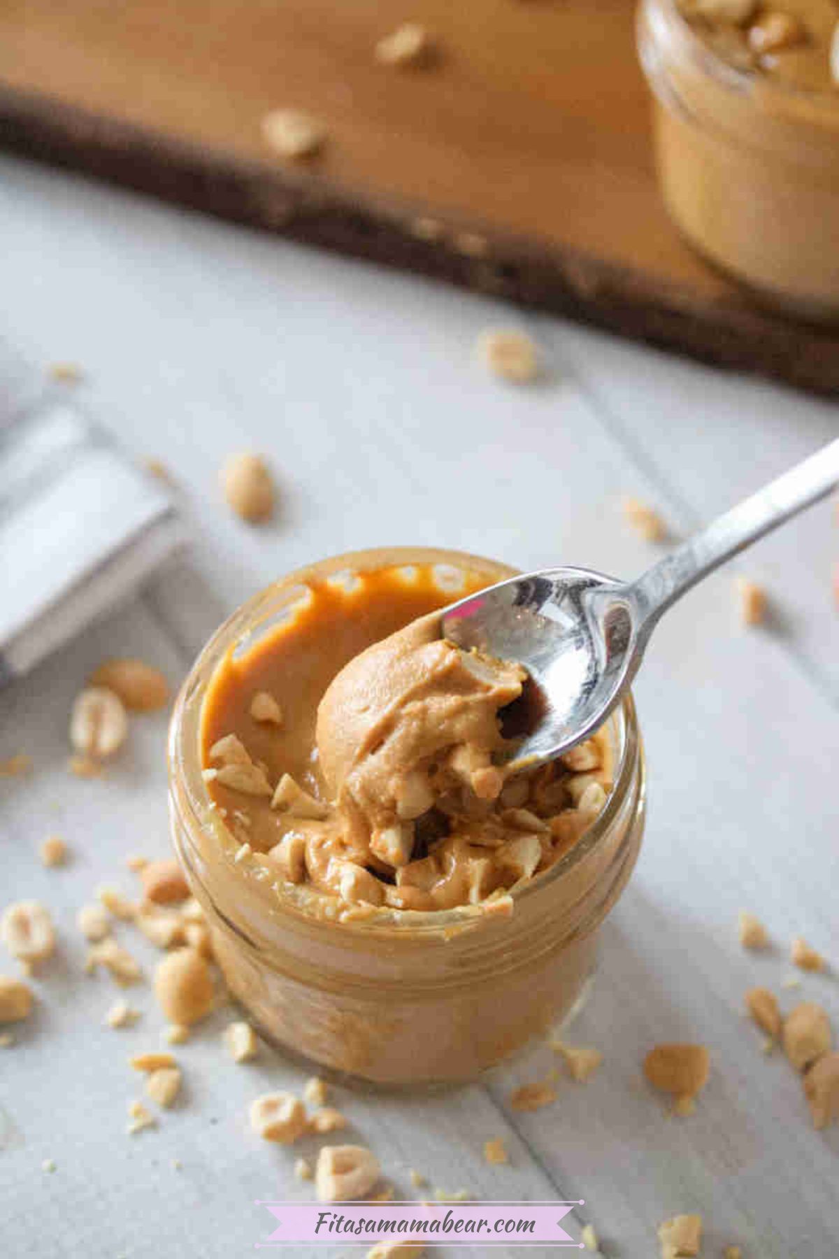Homemade peanut butter in a mason jar topped with peanuts and a spoon and more peanuts around it.