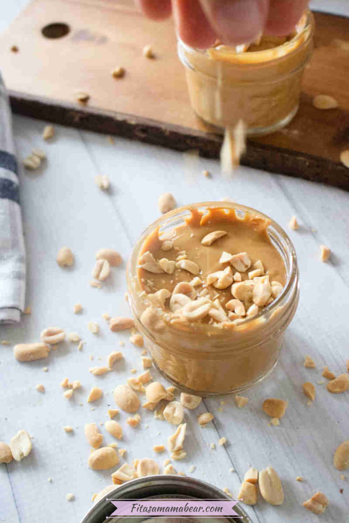 Homemade peanut butter in a mason jar topped with peanuts and more peanuts around it.
