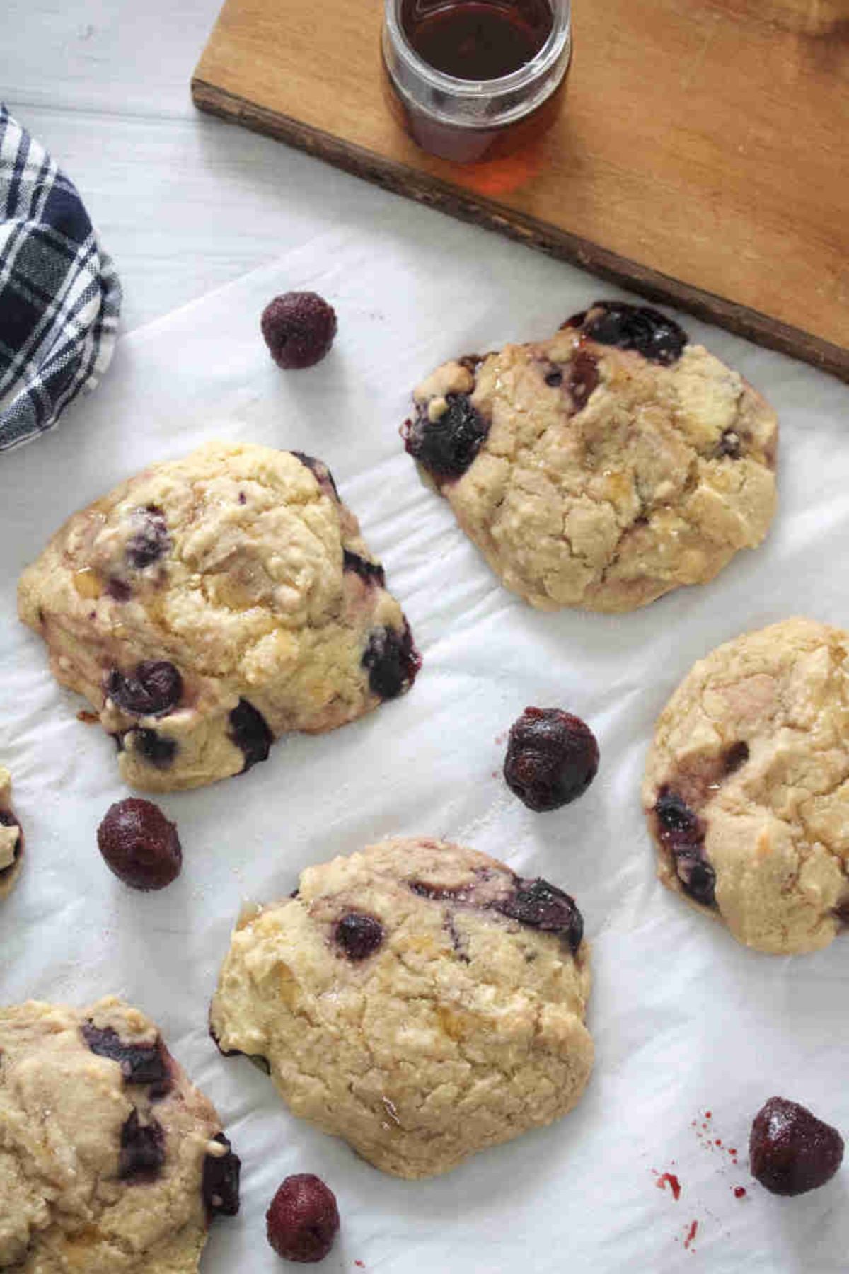 Cherry muffin tops on a piece of parchment paper with frozen cherries around them.