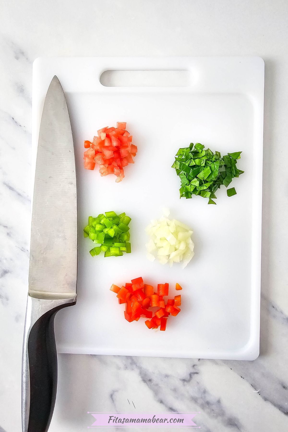 Spinach, tomatoes, onions, and peppers chopped on a cutting board.