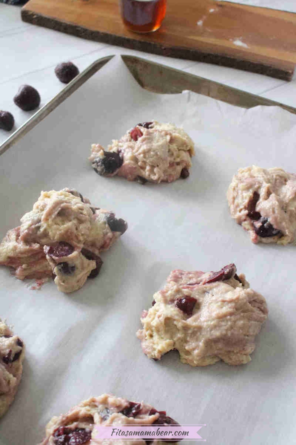 Uncooked muffin tops on a piece of parchment paper with frozen cherries around them.