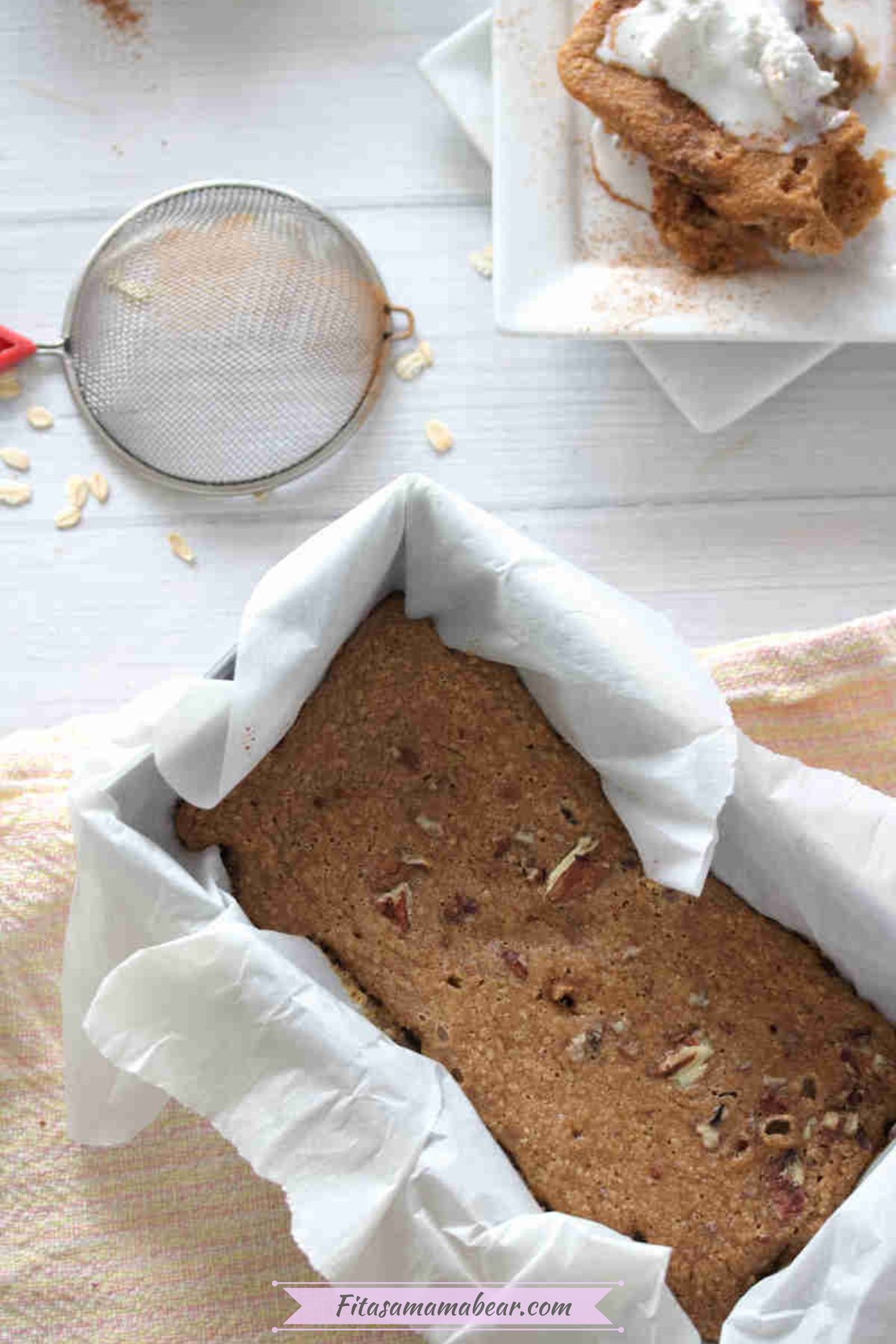 Baked oats in a baking pan lined with parchment paper with a strainer beside it and a plate of sliced baked oats.