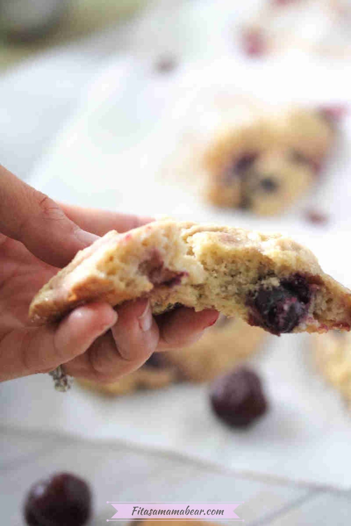 A hand holding a cherry muffin top that's been bitten into.