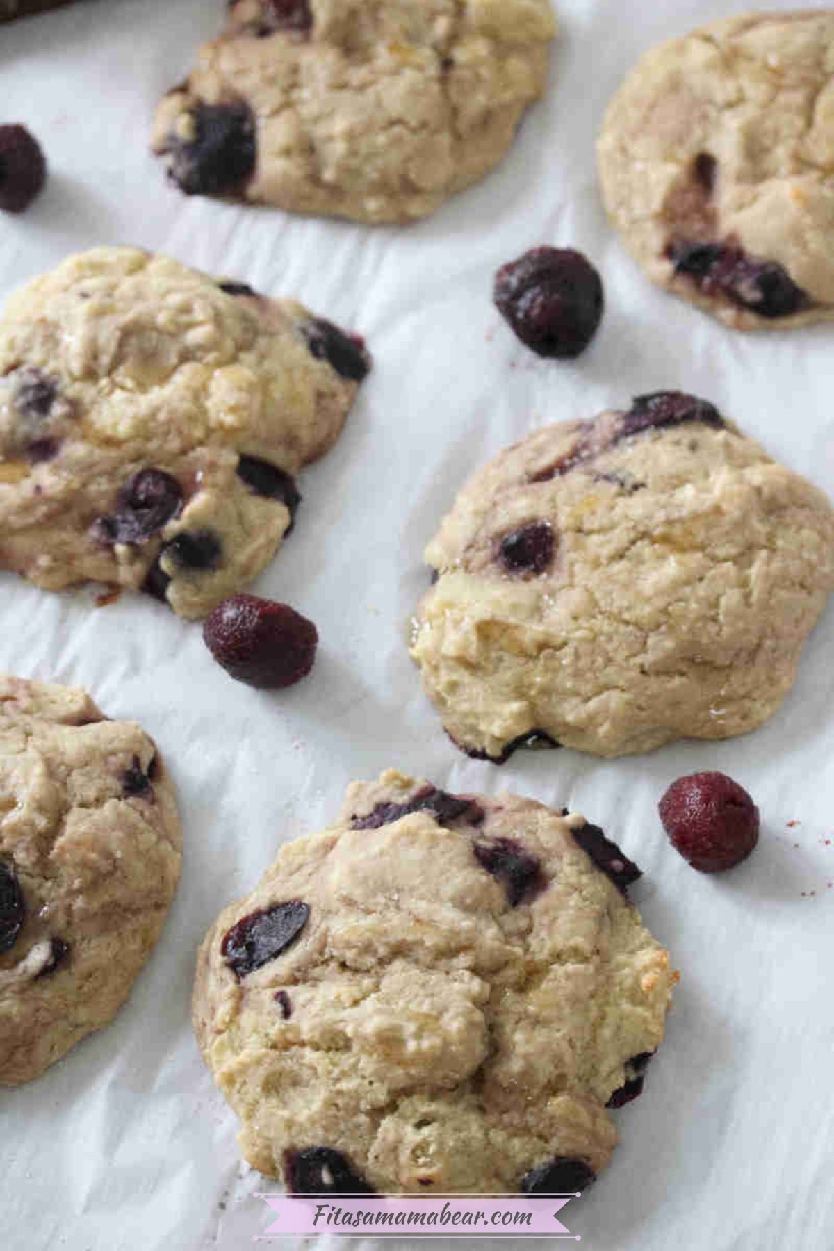 Cherry muffin tops on a piece of parchment paper with frozen cherries around them.