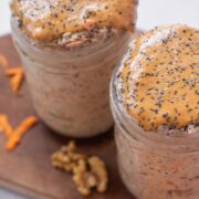 Two mason jars with carrot cake overnight oats topped with nut butter and chia seeds.
