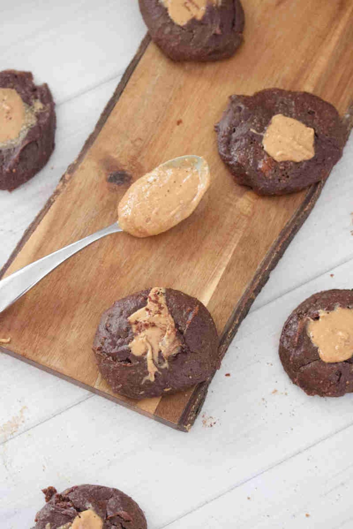 Dark chocolate peanut butter yogurt cookies on top of a wooden board with a spoon of peanut butter.