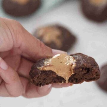 A hand holding half a piece of greek yogurt chocolate cookie with peanut butter toppings.
