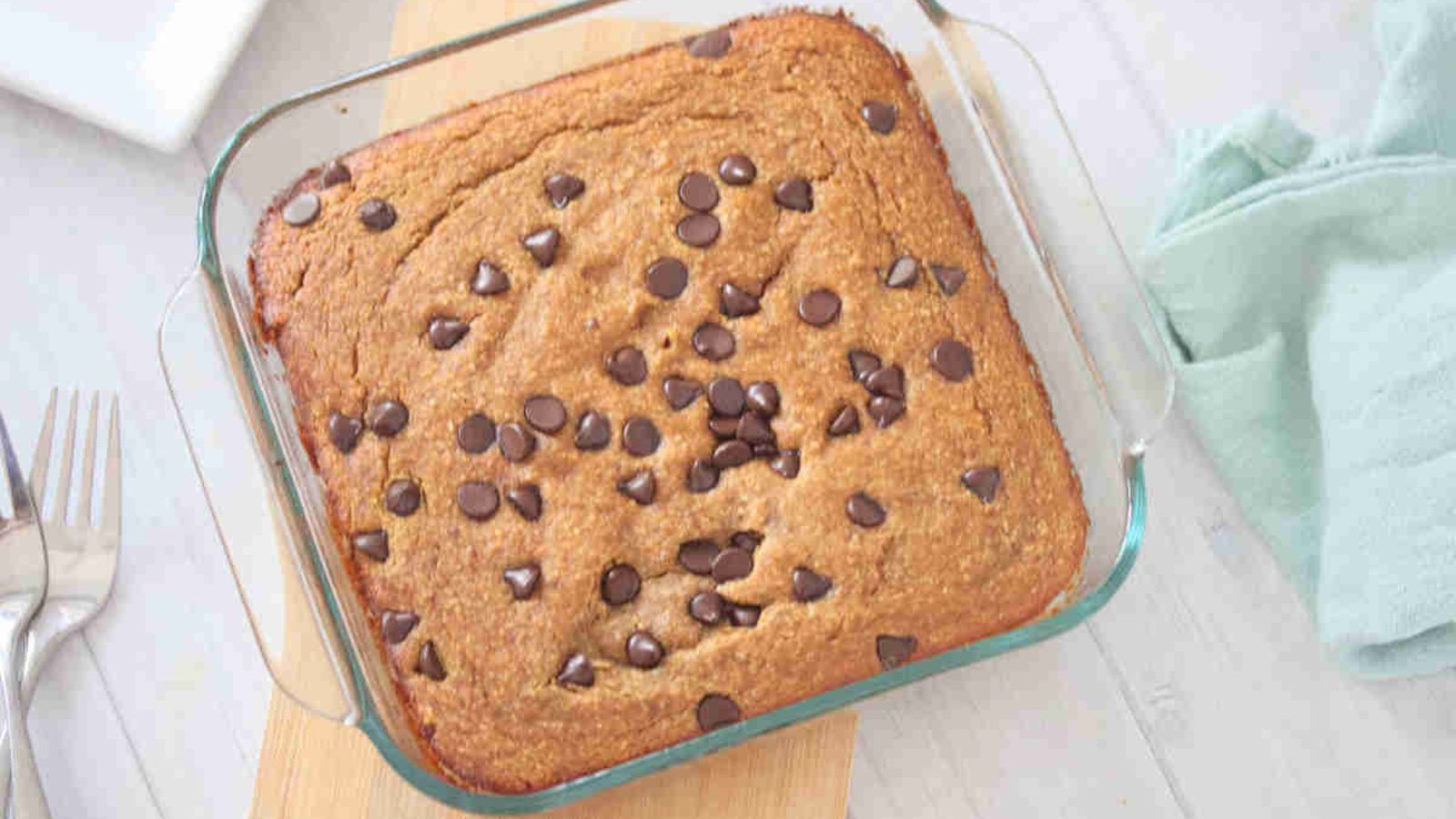 Baked pumpkin oats in a baking dish on top of a wooden board with kitchen towel on the side.