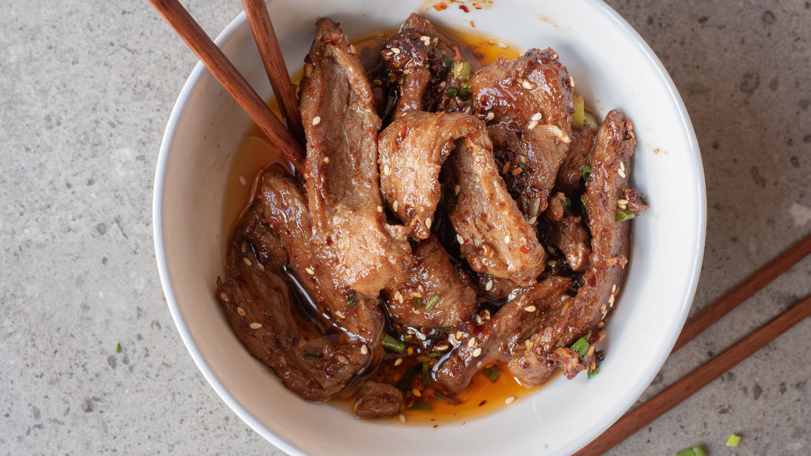 A bowl of stir fried spicy beef strips with chopsticks.