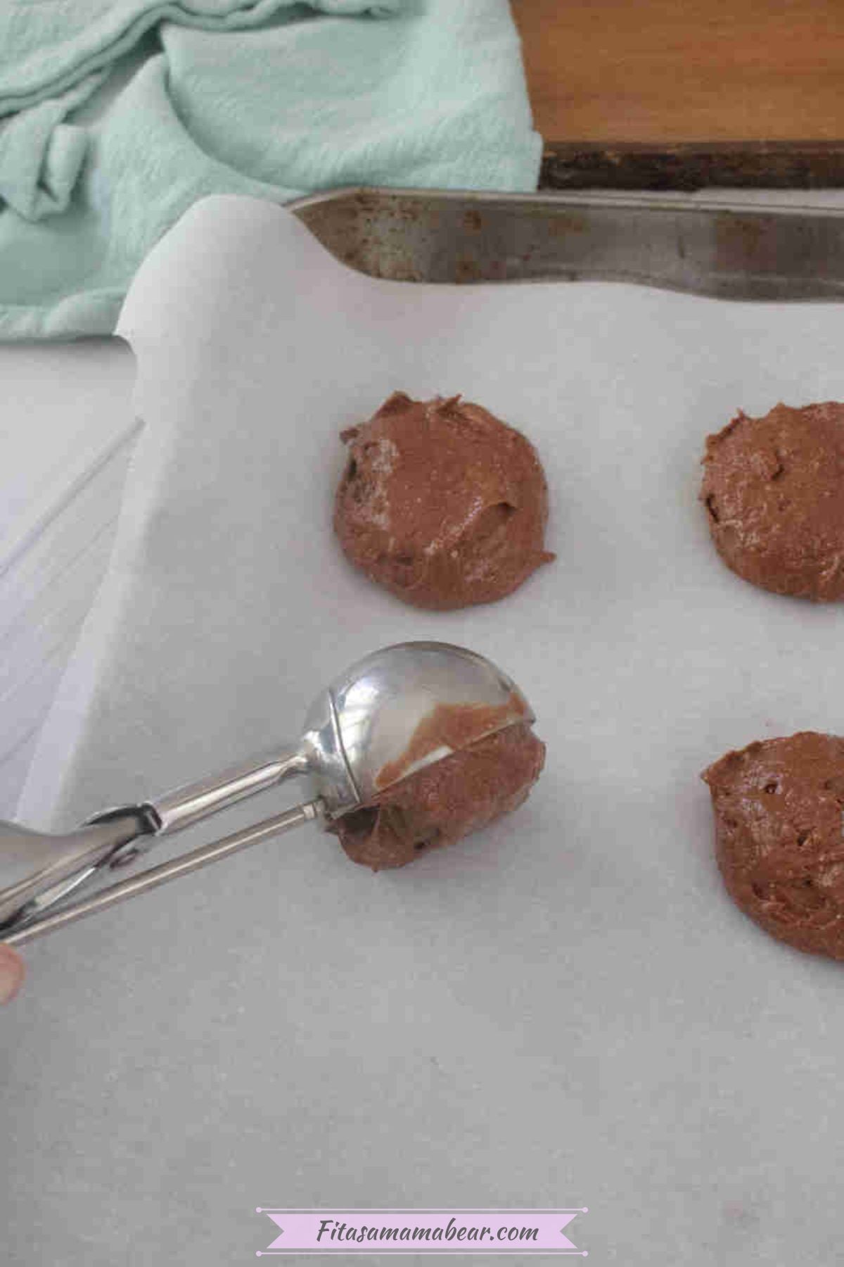 Dark chocolate cookie mixture being scooped into a baking pan with parchment paper.