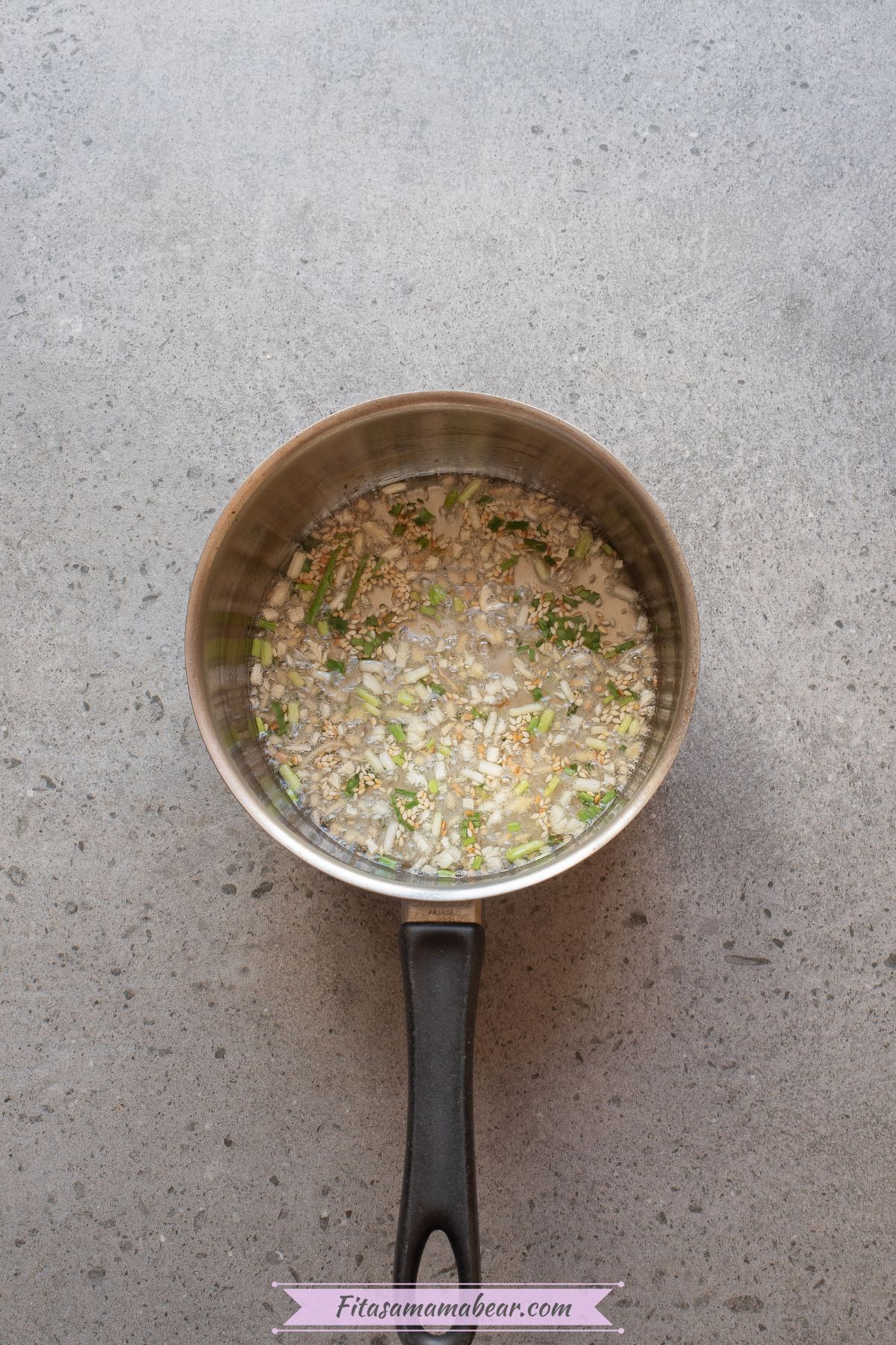 Garlic, green onions, ginger, and sesame seeds being sauteed in a skillet.