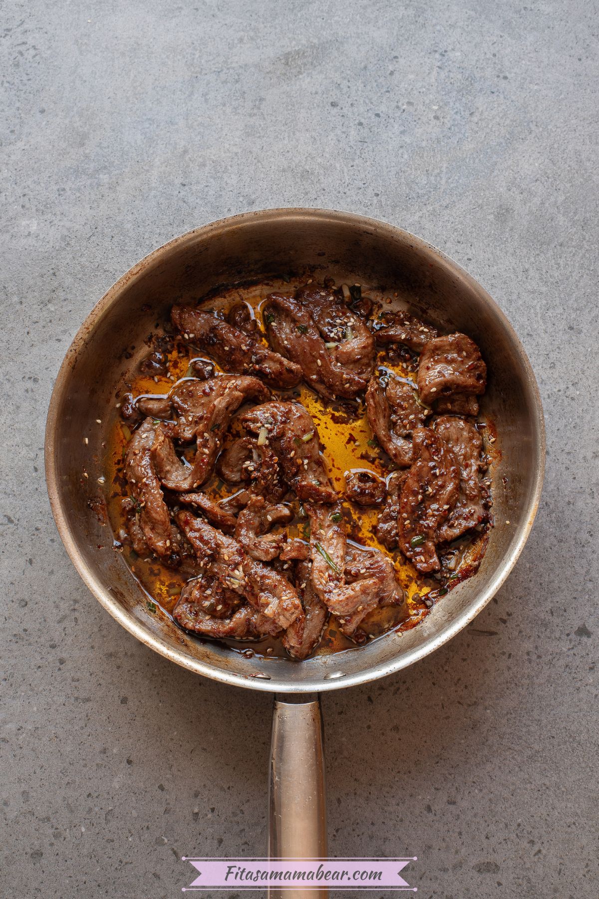 Seared beef strips with chili sauce in a pan.