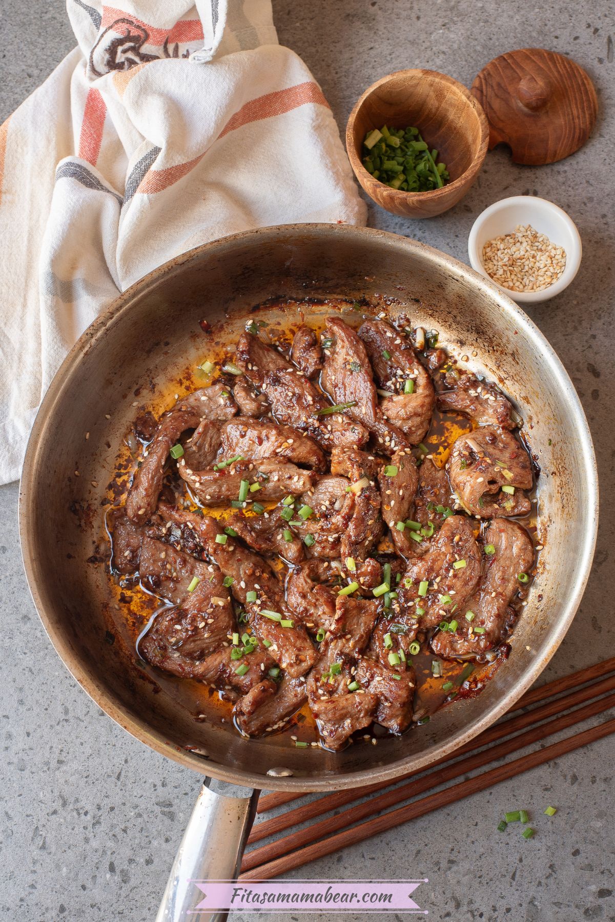 Seared and stir fried beef with chili in a pan with a small bowl of sesame seeds and green onions.