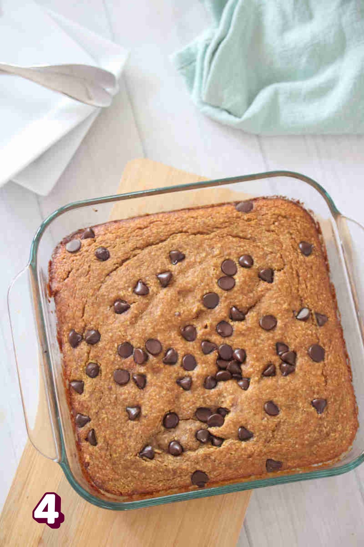 Baked pumpkin oats in a baking dish placed on top of a wooden board with a kitchen towel at the top side.
