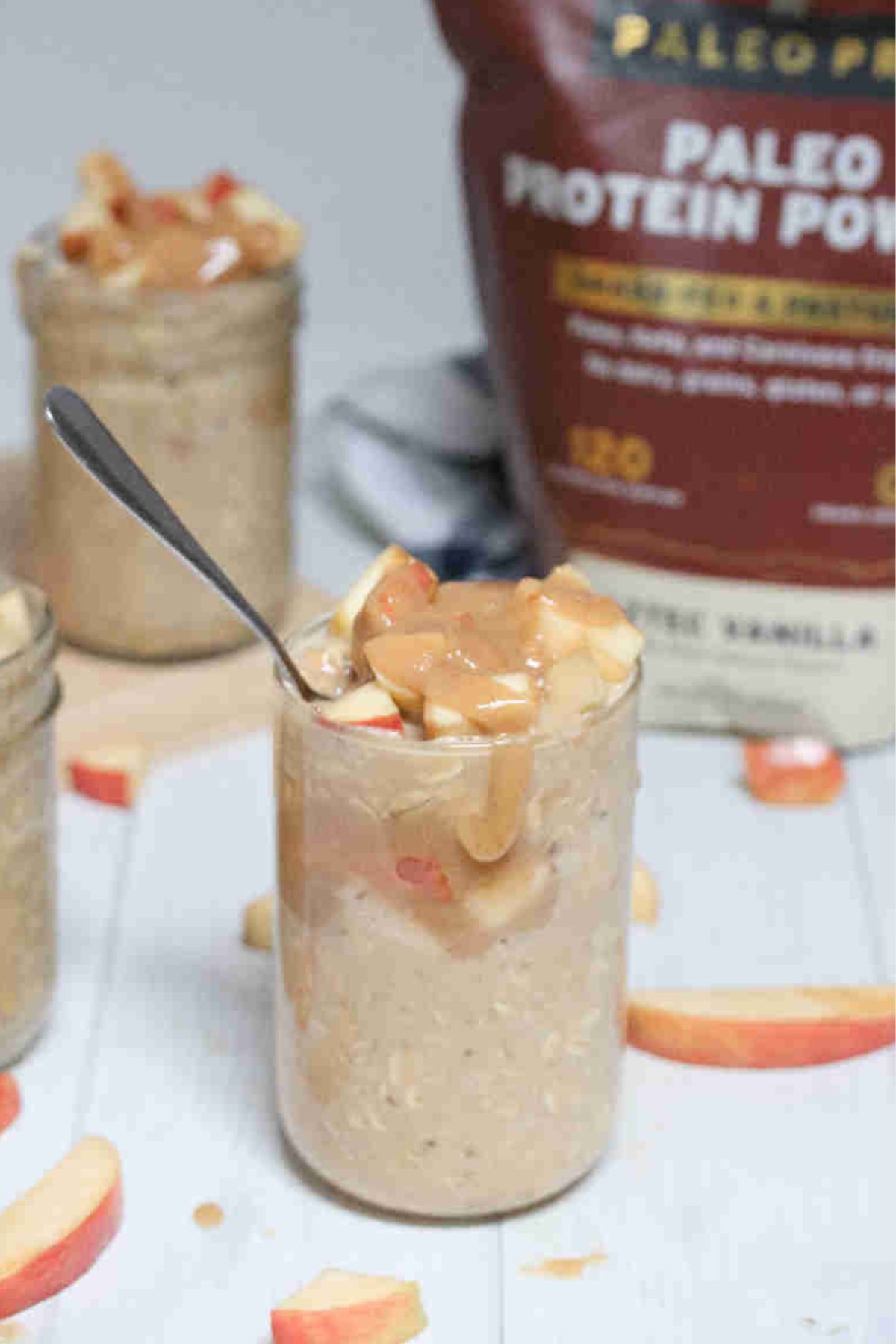Caramel apple overnight oats in mason jars topped with homemade caramel and apples and protein powder in the back.