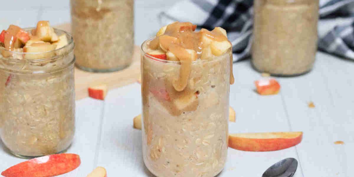 Caramel apple overnight oats in mason jars topped with homemade caramel and apples and sliced apples around them.