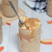Caramel apple overnight oats in mason jars topped with homemade caramel and apples and a spoon in the first jar.