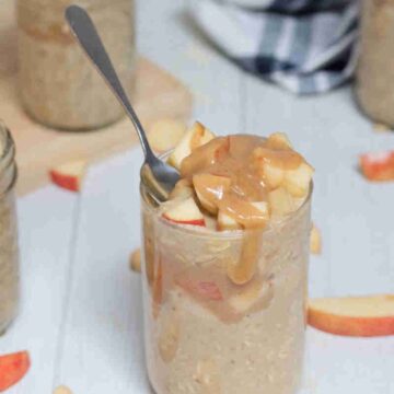 Caramel apple overnight oats in mason jars topped with homemade caramel and apples and a spoon in the first jar.