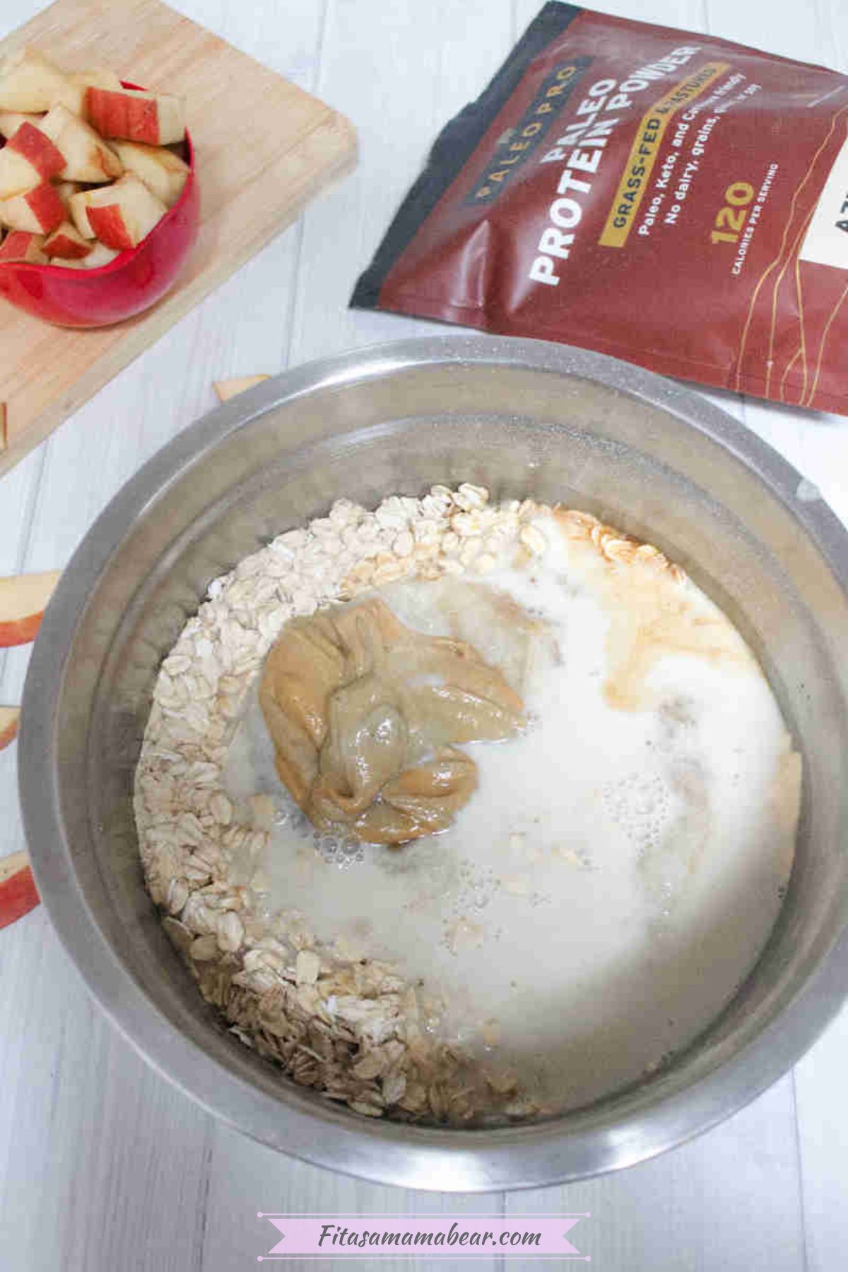Steel bowl with oats, almond butter, milk, and protein powder with protein powder behind it.