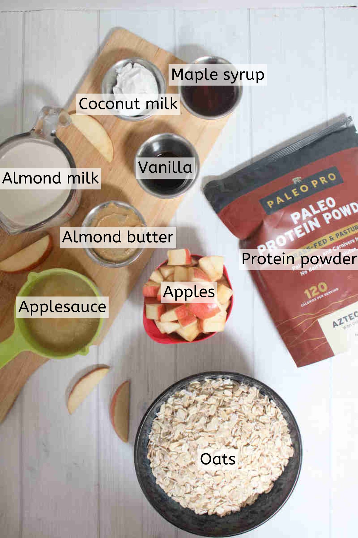 Multiple ingredients to make apple overnight protein oats in measuring cups with text labels over them.