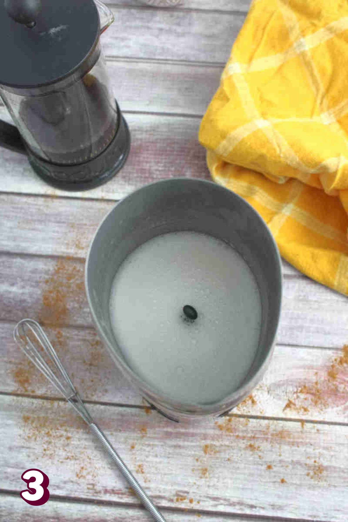 Milk being frothed in a machine with a whisk beside it.