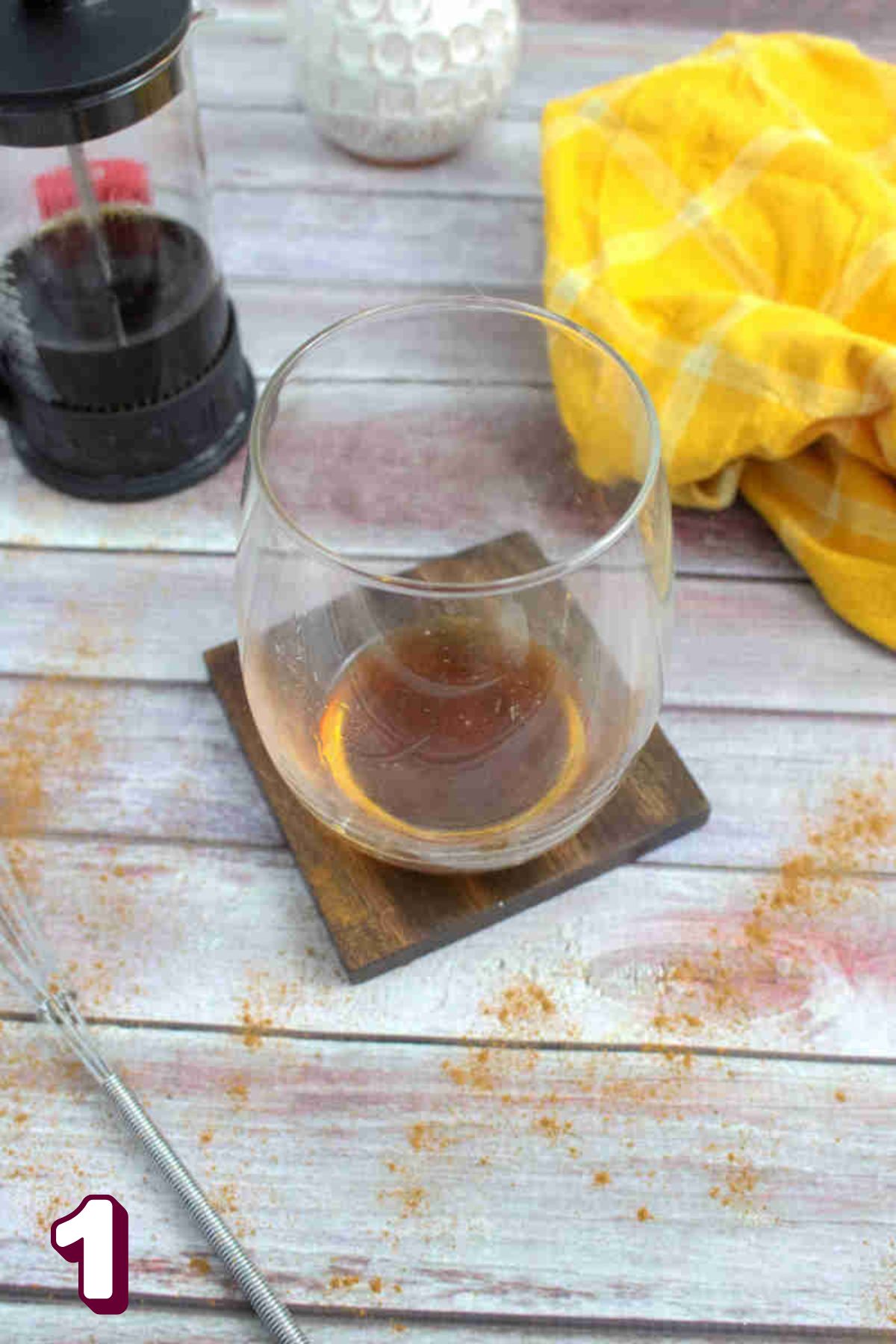 Maple syrup and vanilla in a glass on a wooden coaster.