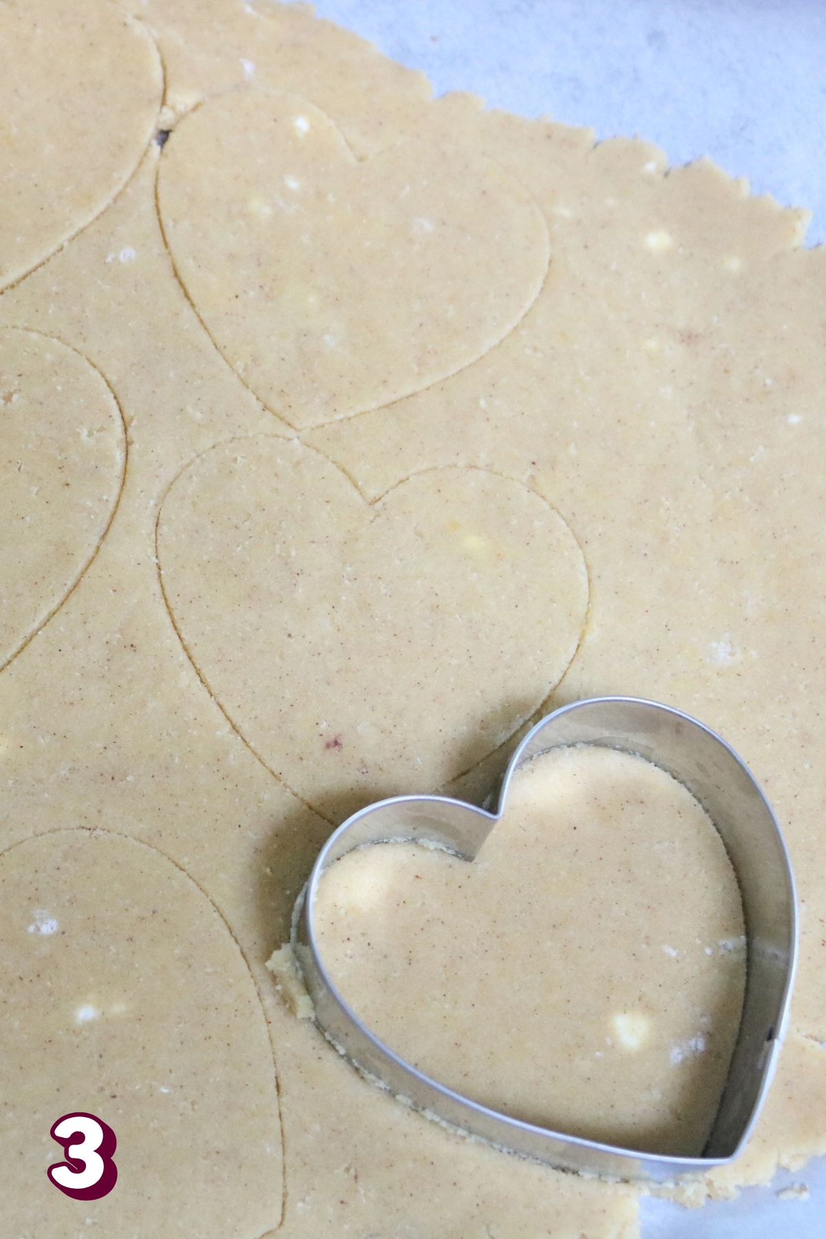 Heart cookie cutter cutting shapes on rolled coconut flour cookie dough.