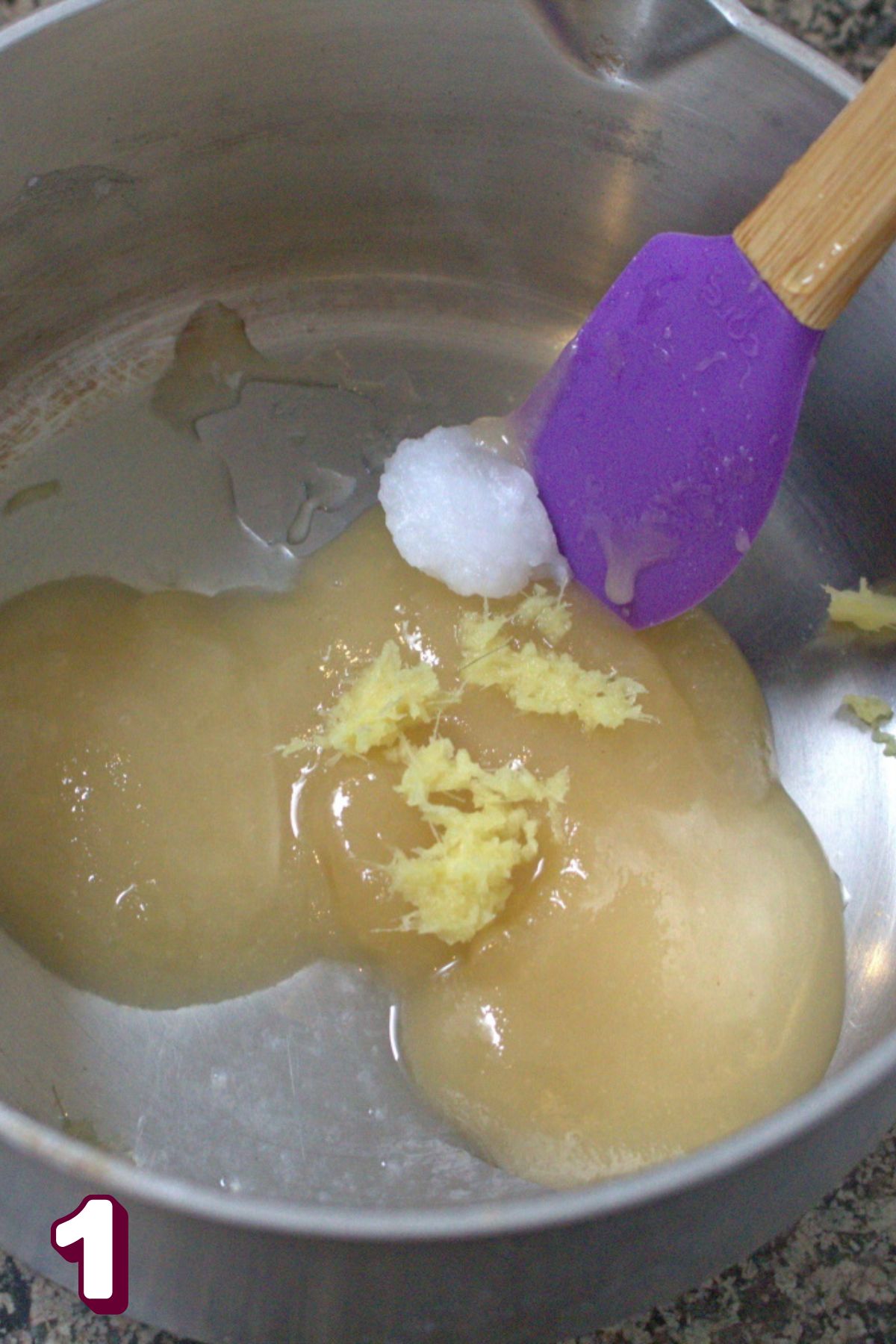 Coconut oil, honey, lemon, and ginger in a small pot with a purple spatula.