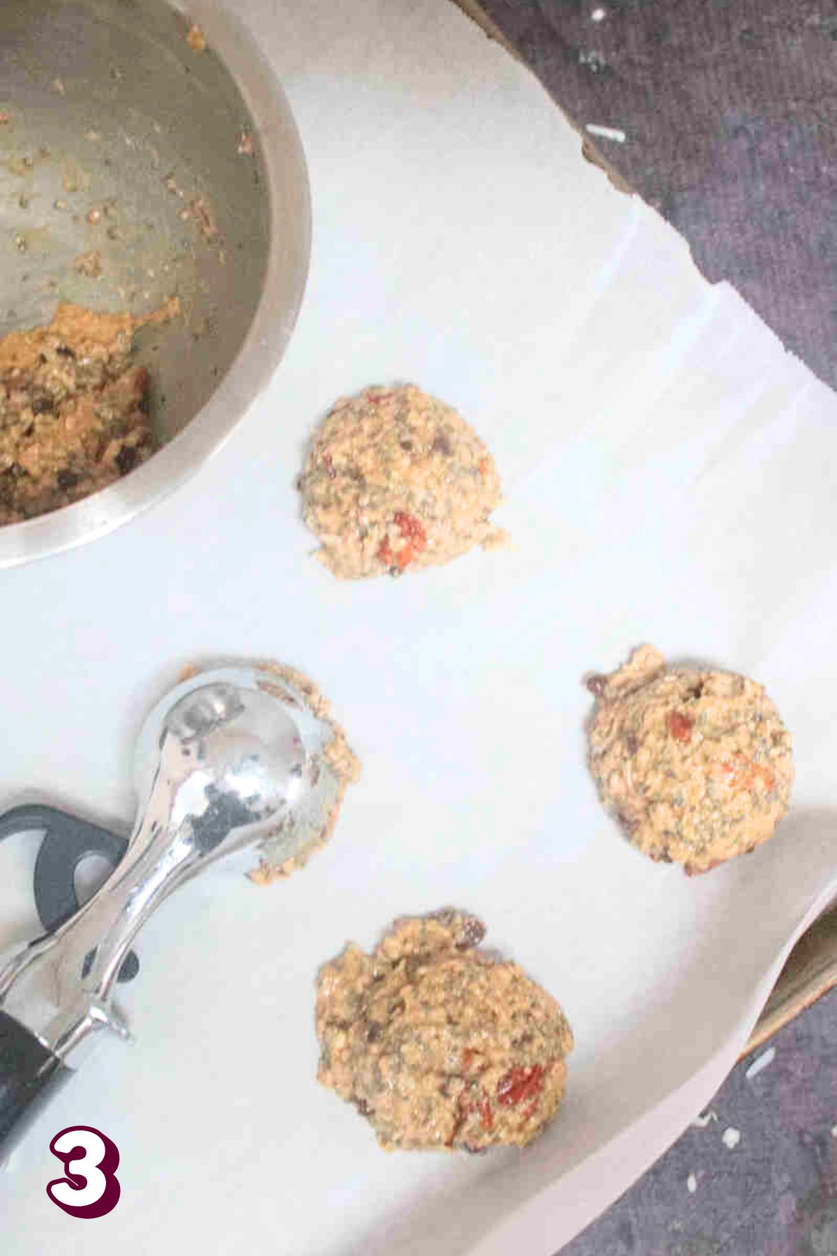 Vegan protein cookies being scooped onto a baking sheet lined with parchment paper.