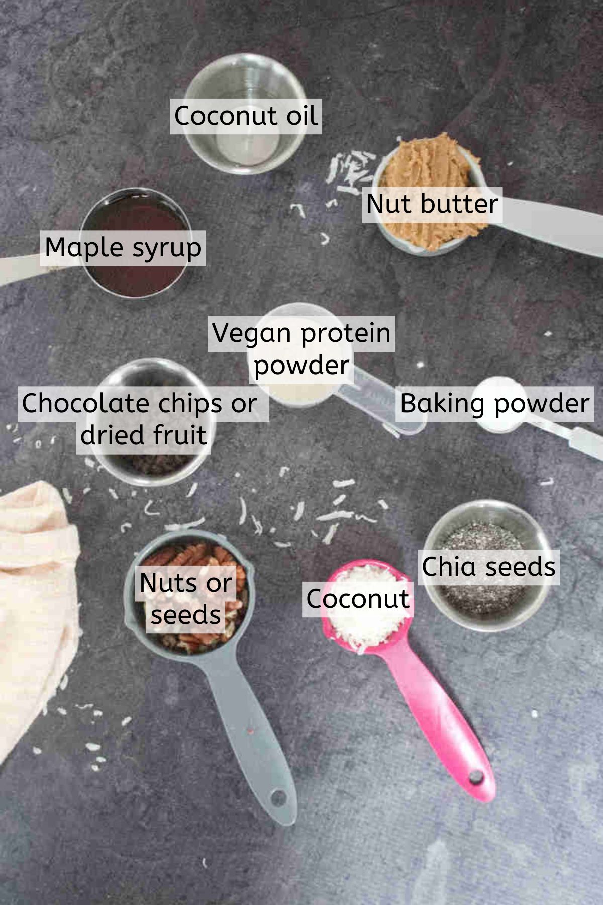 Ingredients like nuts, coconut, chia seeds, and vegan protein powder in measuring cups with text labels over top.