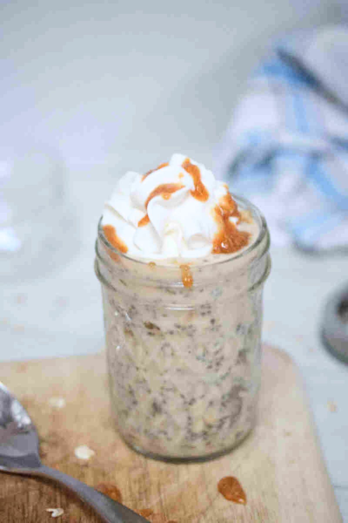 Mason jar with overnight protein powder oats topped with whipped cream and sauce.