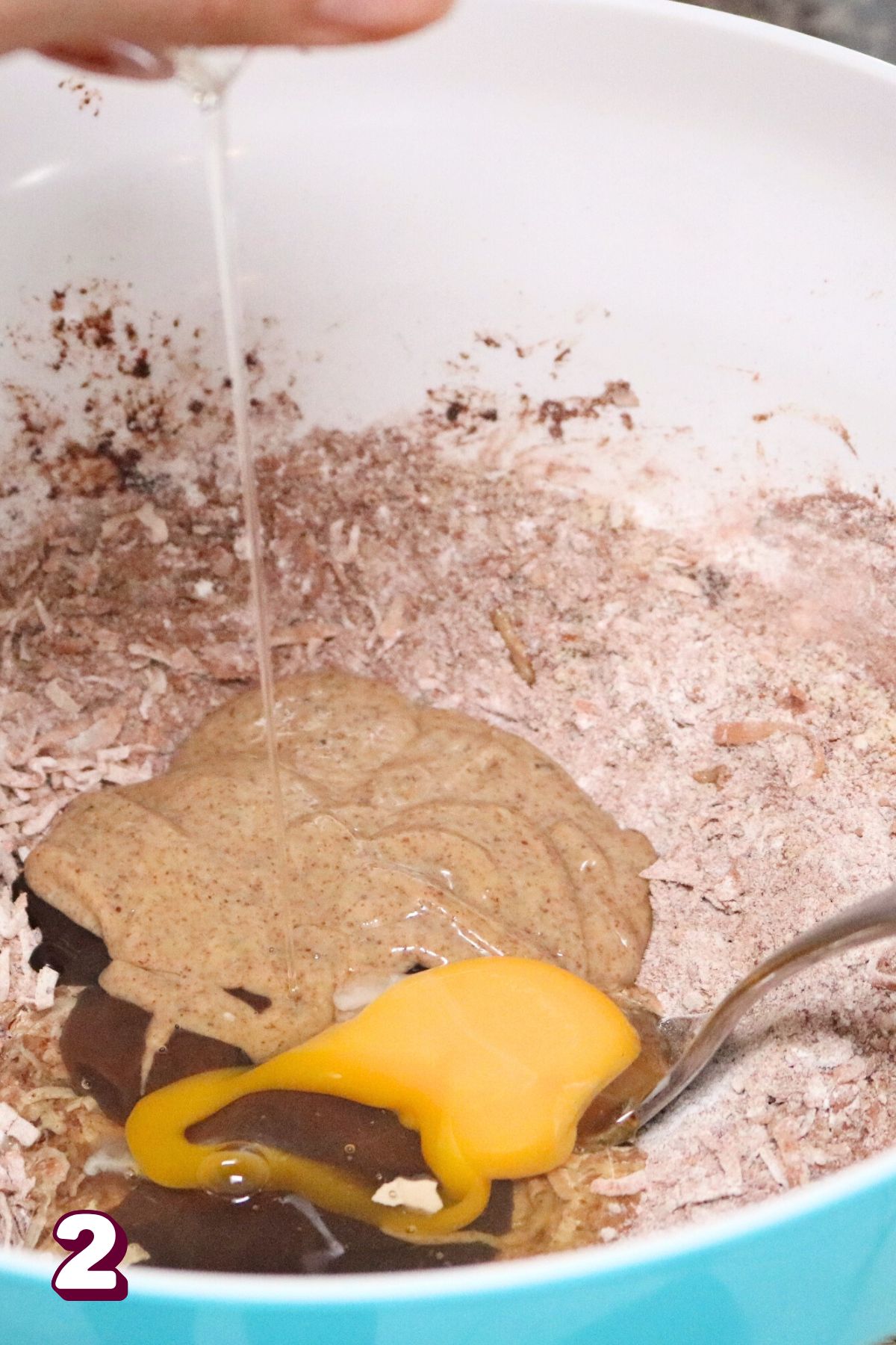 Mixing bowl with coconut, almond flour, and chocolate with an egg and almond butter on top.