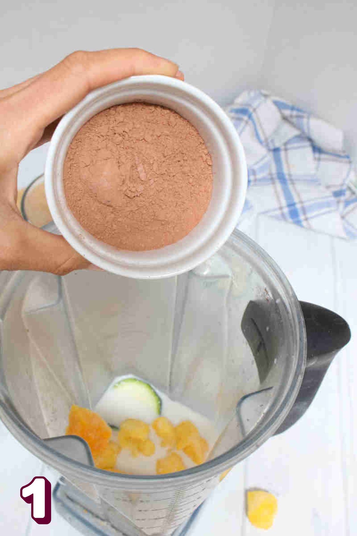 Cacao powder being added to a blender with dates, milk, and zucchini.